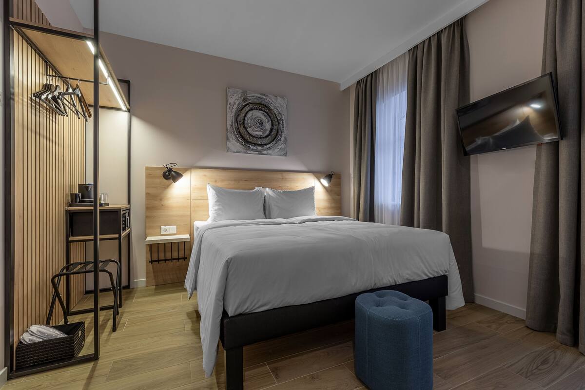 A modern hotel room with a bed, a TV, a desk, and a chair.