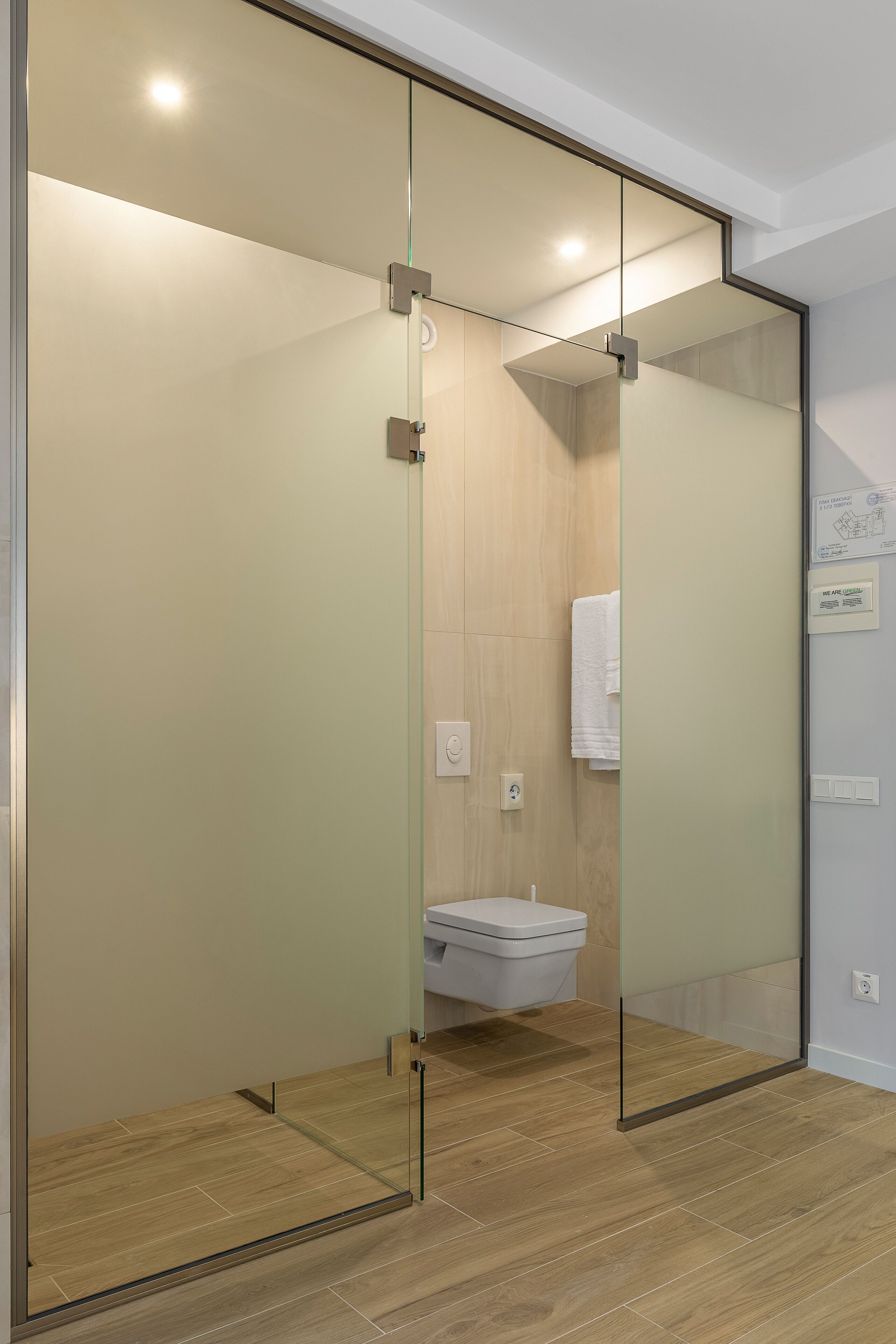 Une salle de bain moderne avec une paroi en verre, un plancher en bois et des toilettes blanches.