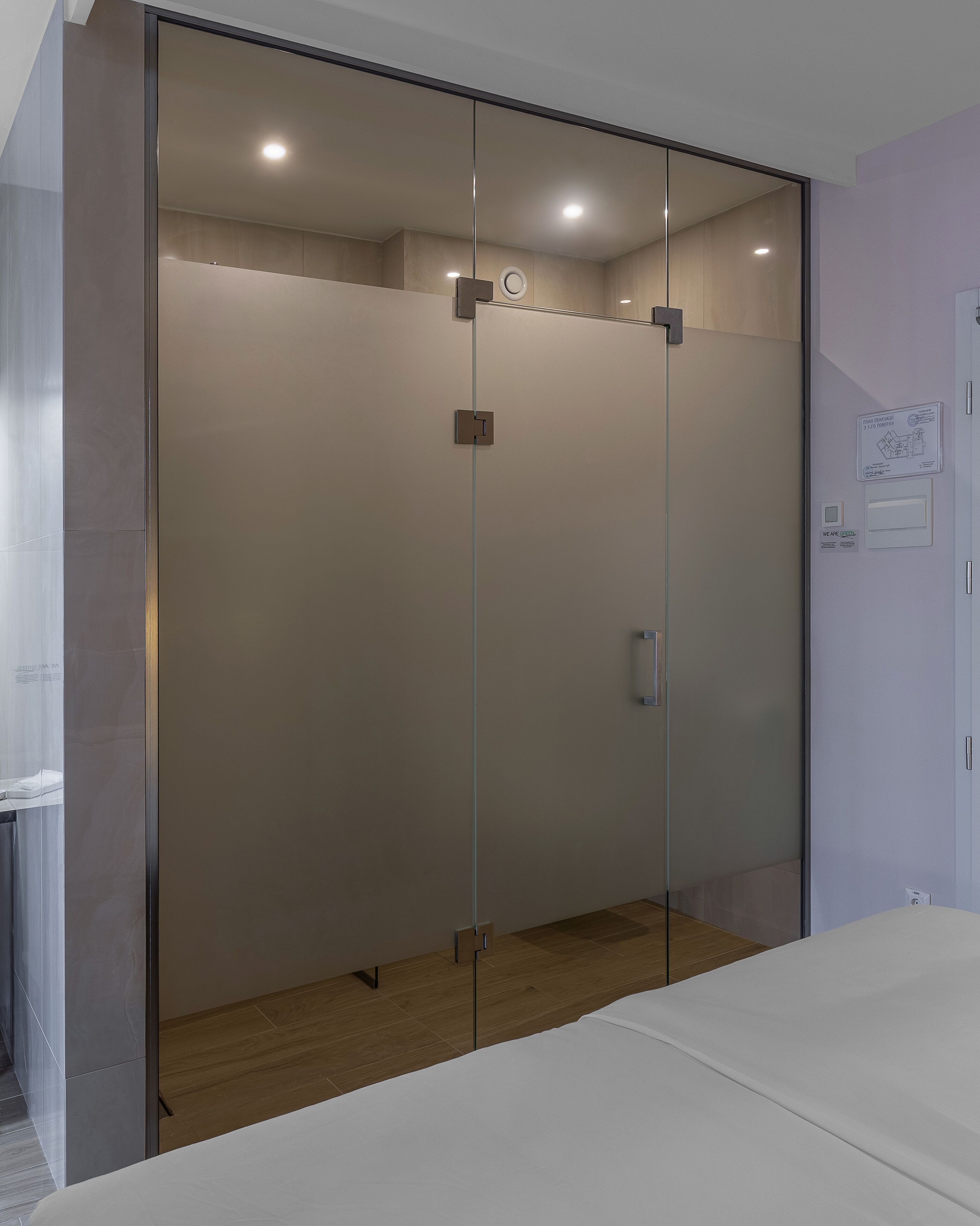 A modern bedroom with a glass wardrobe, a bed, and a wooden floor.