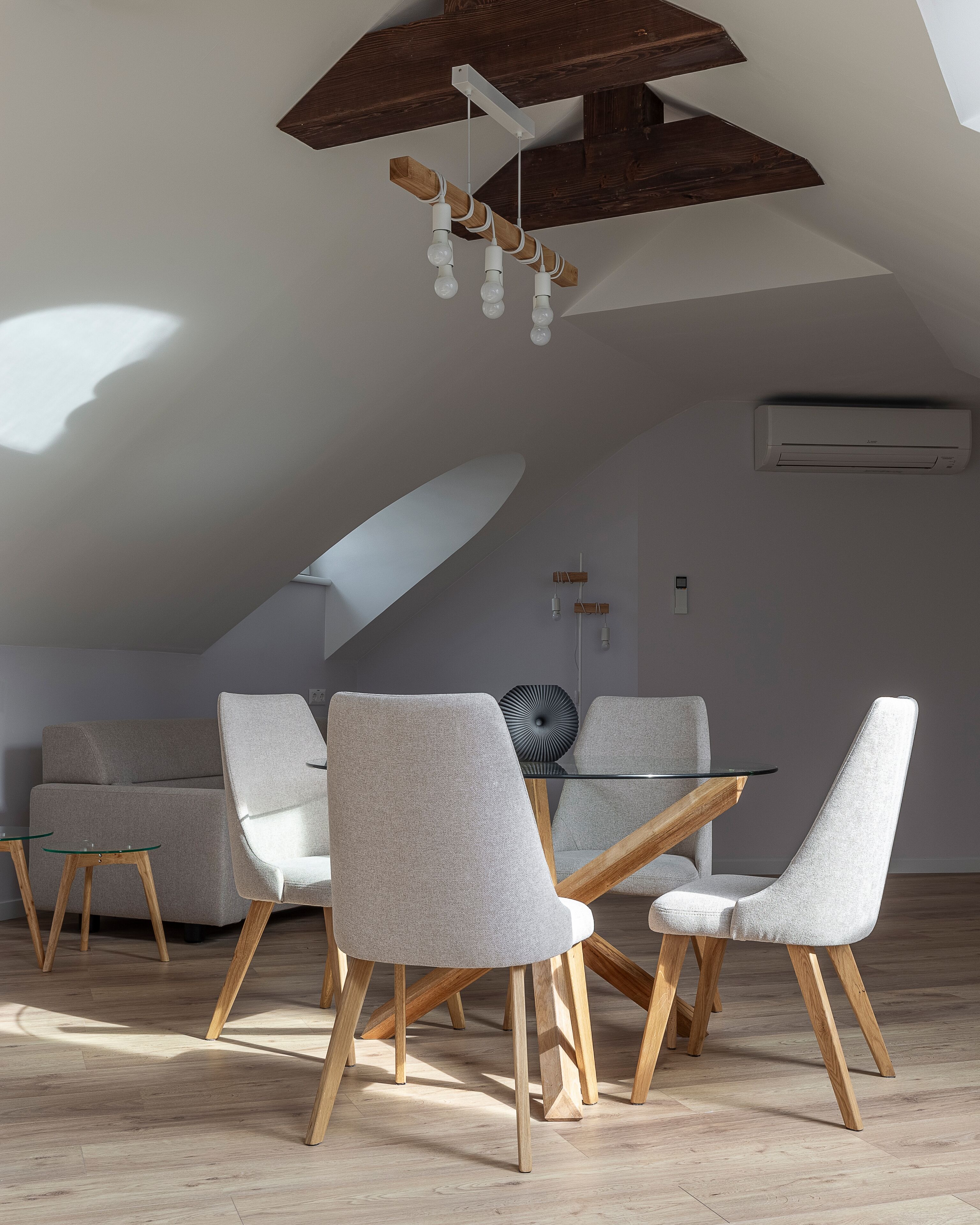 A modern dining area with a glass table, grey upholstered chairs, and wooden legs.