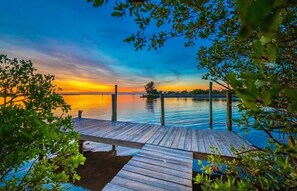 A wooden dock extending into calm water with a sunset in the background.