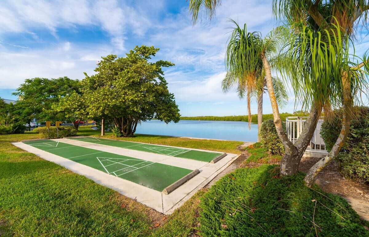 A croquet field with a water body in the background, surrounded by lush greenery and palm trees.