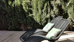 Un fauteuil de relaxation doté d’un coussin et d’un oreiller, placé sur une terrasse en bois, avec en arrière-plan un luxuriant feuillage verdoyant.