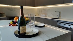 Une cuisine moderne avec un plan de travail en marbre, une bouteille de champagne brut nature et un verre posé sur un sous-verre noir.