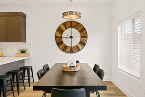 A dining area with a large wooden table, six chairs, a round wall clock, and a hanging light fixture. - Large Home Sleeps 16-Pool Perfect For Family Fun! (St. George)