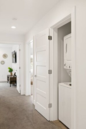 A hallway with white doors, a small table with a plant, and a washing machine. - Large Home Sleeps 16-Pool Perfect For Family Fun! (St. George)