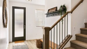 A modern interior with a wooden staircase, a welcome sign, a door with blinds, and a basket on the floor. - Large Home Sleeps 16-Pool Perfect For Family Fun! (St. George)