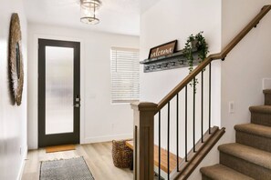 A modern interior with a wooden staircase, a welcome sign, a door with blinds, and a basket on the floor. - Large Home Sleeps 16-Pool Perfect For Family Fun! (St. George)