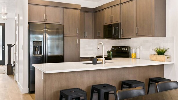 A modern kitchen with dark wood cabinets, a stainless steel refrigerator, a built-in microwave, and a white countertop. There are three black stools at the island. - Large Home Sleeps 16-Pool Perfect For Family Fun! (St. George)