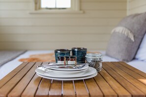 A wooden table with a white plate, two wooden spoons, and two jars of jam. - Rumwold by Bloom Stays -  a rural shepherds hut sleeping 2 with amazing views! (Ashford)