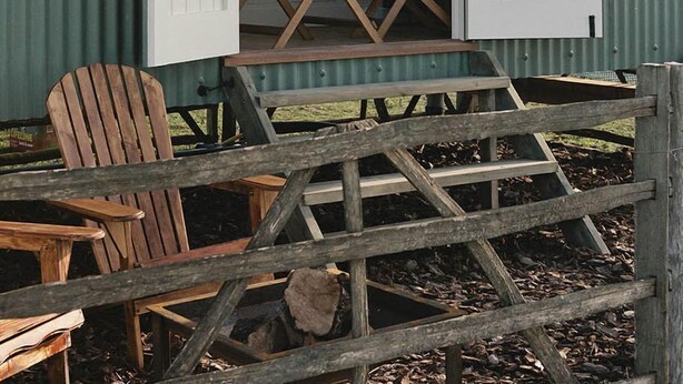 A rustic cabin with a wooden deck, a dining table, and a chair outside. - Rumwold by Bloom Stays -  a rural shepherds hut sleeping 2 with amazing views! (Ashford)