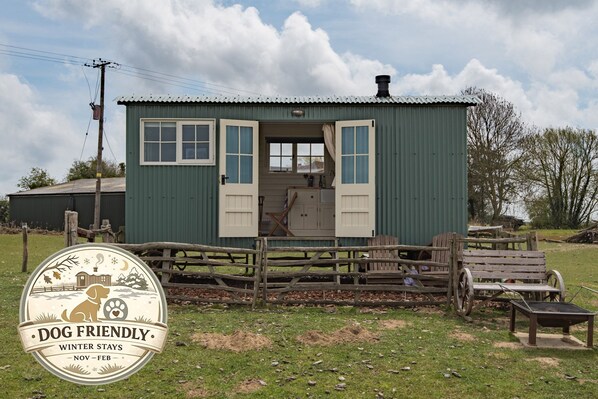 A rustic cabin with a wooden fence, a bench, and a table outside. - Rumwold by Bloom Stays -  a rural shepherds hut sleeping 2 with amazing views! (Ashford)
