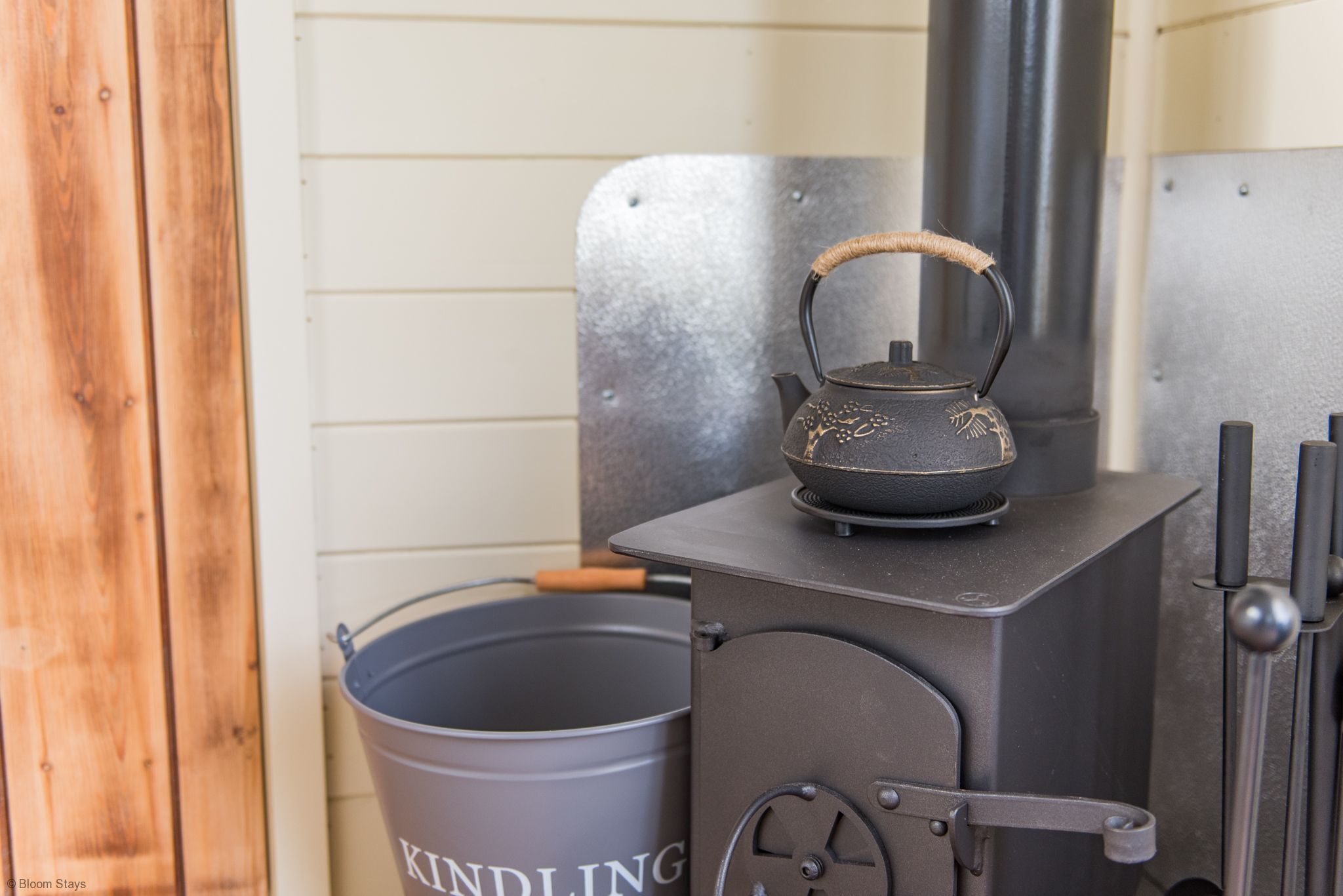 En brændeovn med en kedel ovenpå, en balje mærket 'KINDLING' og en ståldør.