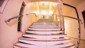 A spiral staircase with white steps and metal railings, leading to a landing with a chandelier. - Hotel Tito's (Capanema)
