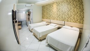 A hotel room with three single beds, a small seating area, and a patterned wallpaper on the wall. - Hotel Tito's (Capanema)
