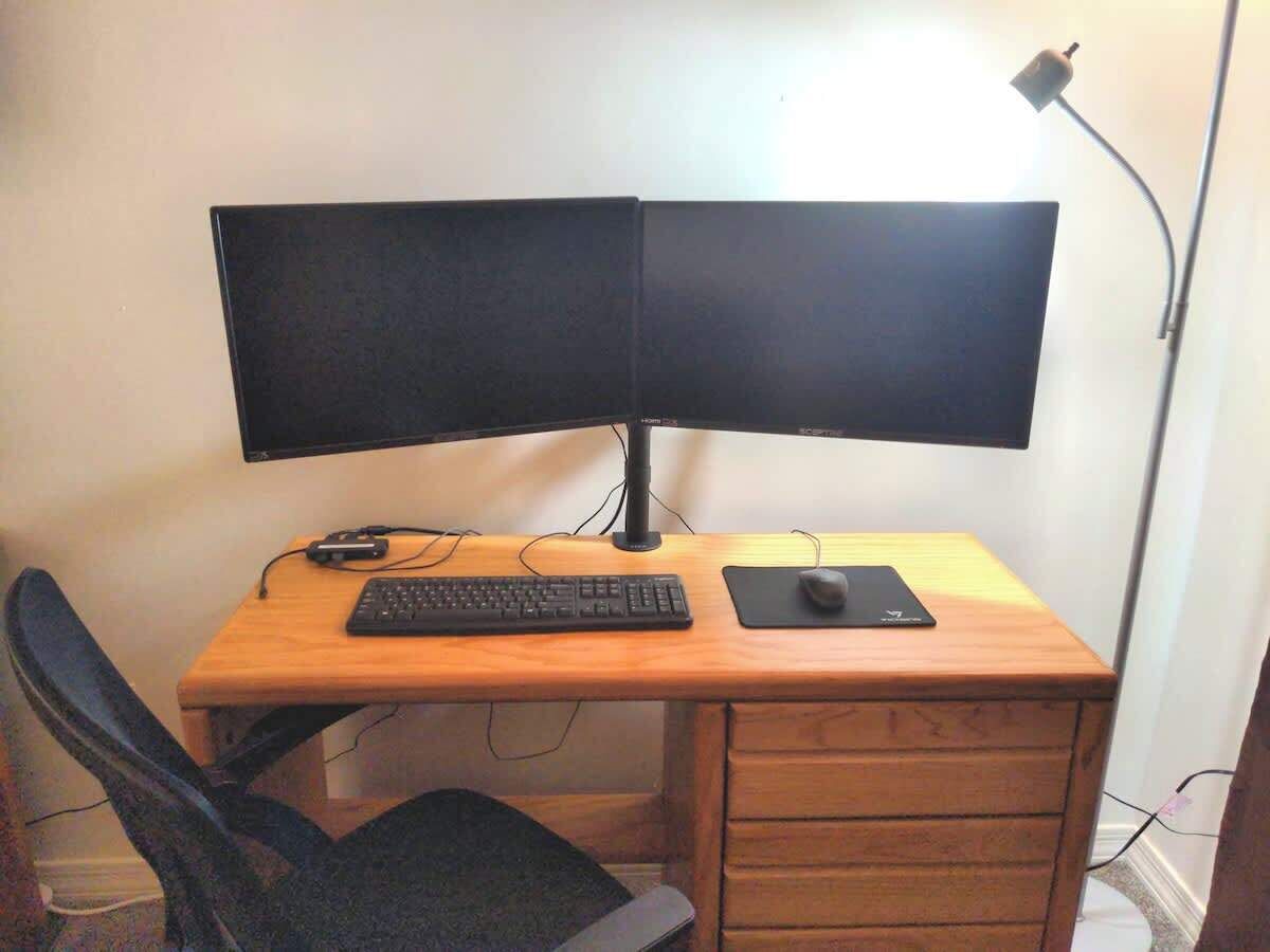 A wooden desk with a dual monitor setup, a keyboard, a mouse, and a lamp.