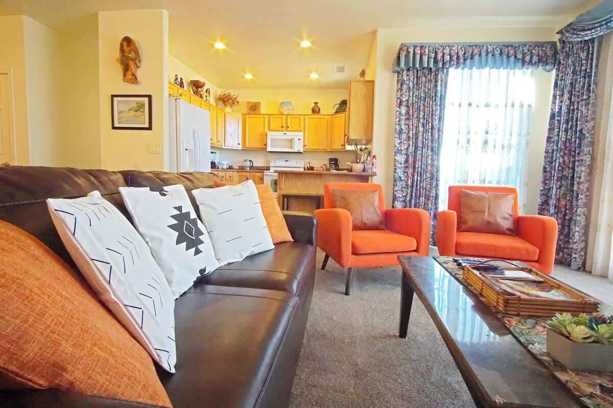 A living room with a sofa, two armchairs, a coffee table, and a kitchen in the background.