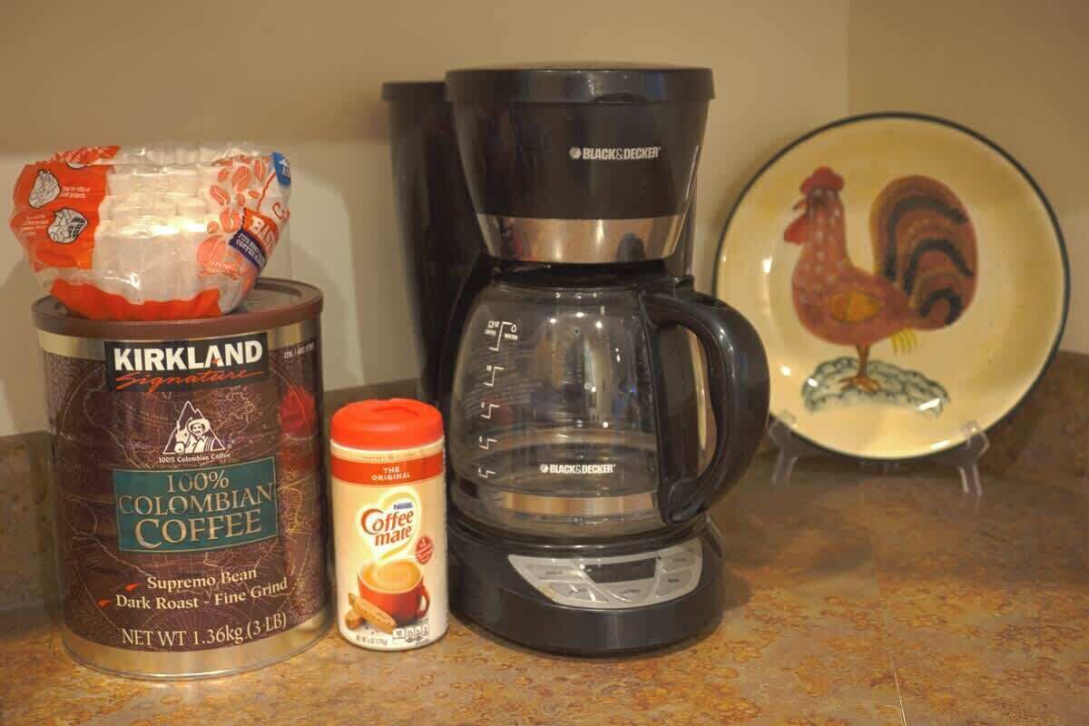 A coffee maker, a can of coffee, and a coffee bag on a kitchen counter.