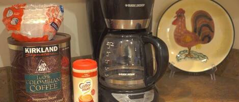 A coffee maker, a can of coffee, and a coffee bag on a kitchen counter.