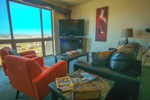 Una sala de estar con un ventanal grande, un televisor de pantalla plana, un sofá y una mesa de centro con revistas.