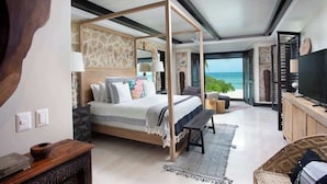 Un'ampia camera da letto con un letto a baldacchino, una grande finestra vista sull'oceano e un televisore su un mobile in legno.