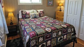 Un dormitorio con colcha acolchada, una ventana, un aparador y una puerta.
