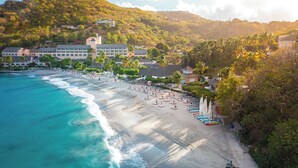 Un resort en la playa con una orilla arenosa, un edificio de hotel y palmeras.