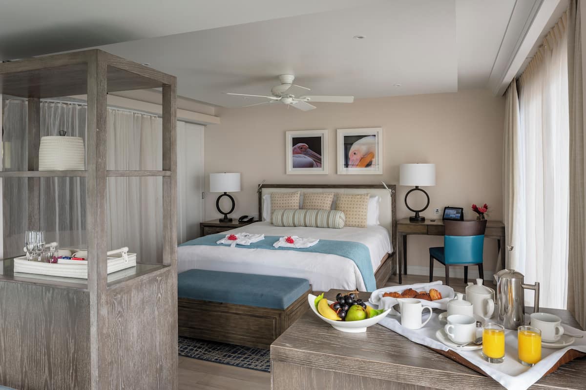 A hotel room with a bed, bedside tables, a desk, and a breakfast tray with fruits and beverages.