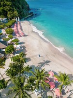 Un resort frente a la playa con piscina, sillones de descanso y sombrillas.