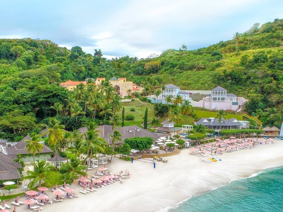 Una propiedad frente a la playa con varias construcciones, una playa de arena y abundante vegetación.