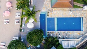 Vista aérea de un resort con piscina, sillas de descanso y palmeras.
