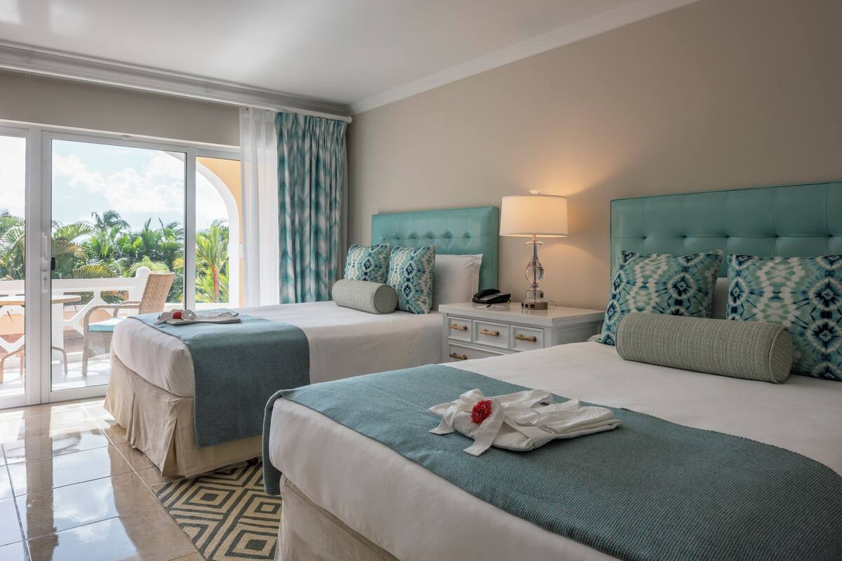 A hotel room with two beds, a balcony, and a view of the outdoors.