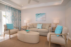 A living room with a beige sofa, two armchairs, a coffee table, and a large window with curtains.