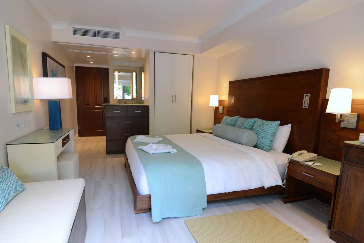 A hotel room with a bed, bedside tables, a desk, a mirror, and a wardrobe.