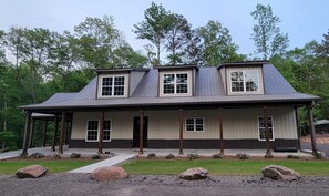 A two-story house with a covered porch, large windows, and a metal roof.