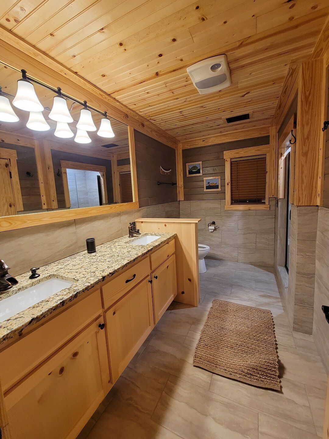 Casa de banho de cabana de madeira com lavatório em bancada de granito, armários de madeira, um espelho grande e área de duche.