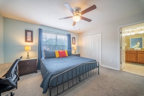 A bedroom with a bed, a desk, a chair, a ceiling fan, and a window with curtains.