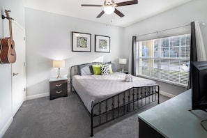 A bedroom with a bed, bedside tables, a guitar, and a window with blinds.