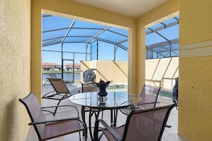 A glass-enclosed patio with a round table and chairs, a vase, and a view of a building and water in the background.
