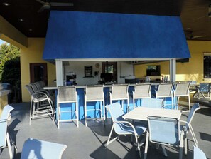 An outdoor seating area with tables and chairs, a counter with kitchen appliances, and a blue awning. - Near Disney, Private Pool, No Rear Neighbors & Front-Door Parking, Gated Resort (Kissimmee)