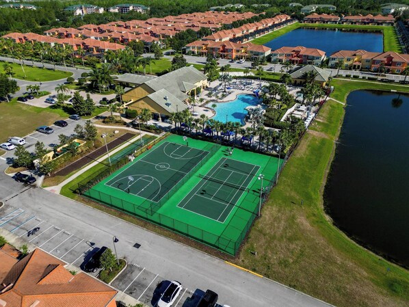 An aerial view of a residential area with a tennis court, swimming pool, and a lake.