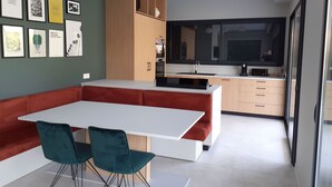 Una cocina moderna con una isla blanca, armarios de madera y un banco rojo. Hay cuadros en la pared y un ventanal sobre el fregadero.