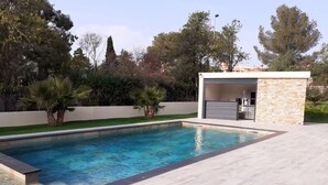 Un área de piscina moderna al aire libre con un muro de piedra y una zona de estar cubierta.