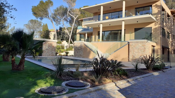 Una casa moderna de dos pisos con piscina, pilares de piedra y un jardín bien cuidado.
