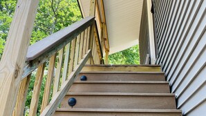 A wooden staircase with metal railings and black round accents, leading to a covered area with a white ceiling.