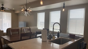 A modern kitchen with a central island, a dining area with a sofa and chairs, and large windows with blinds. - Gorgeous modern Denver townhome close to city center (Denver)