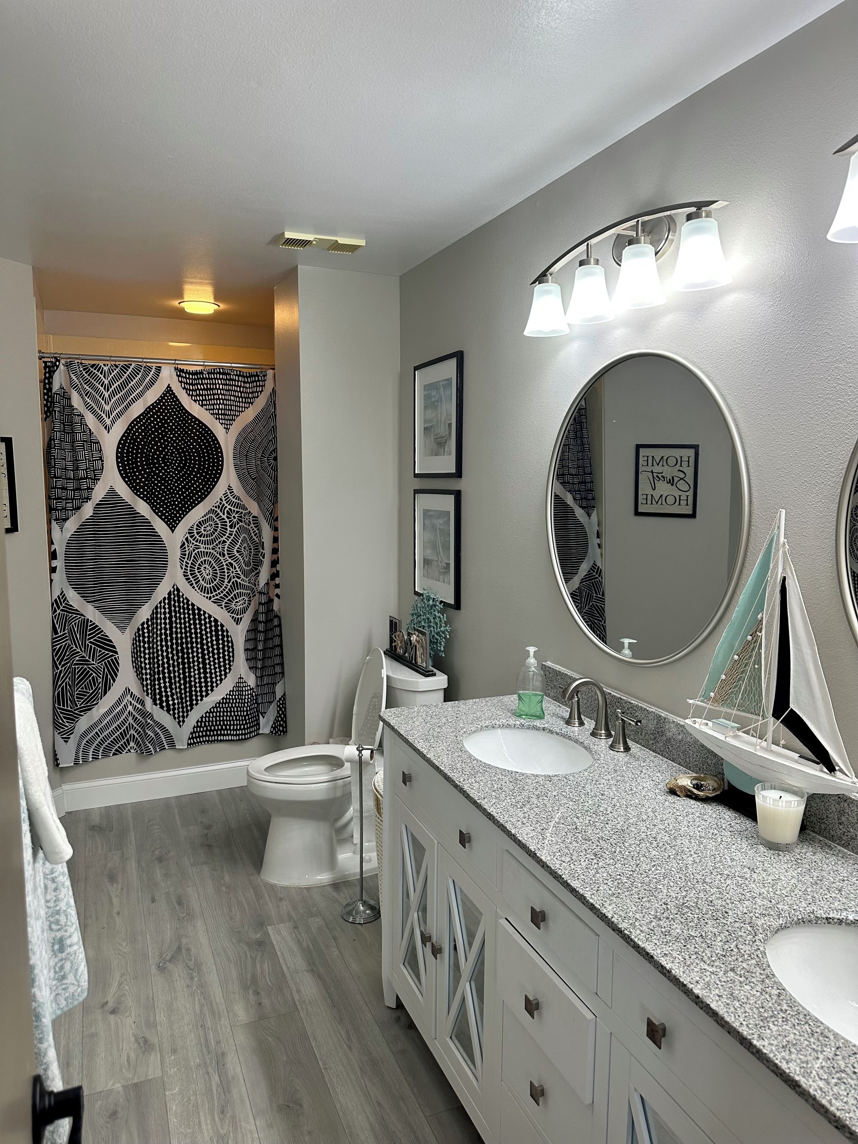 A bathroom with a modern design, featuring a large mirror, two sinks, and a shower area with a patterned curtain.