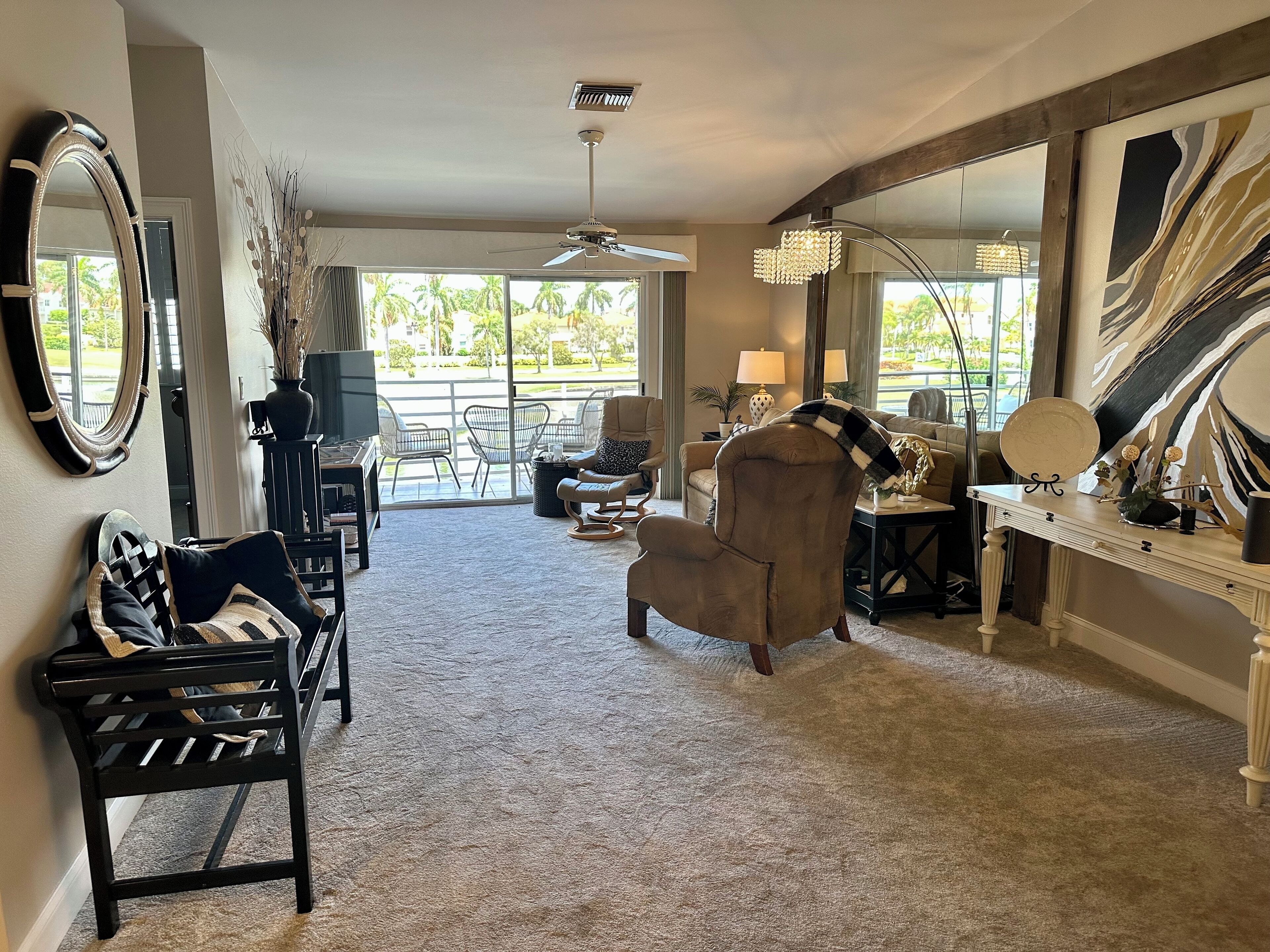 A spacious living room with a large mirror, a ceiling fan, and a view of the outdoors.