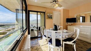 A balcony with a view of a highway and buildings, a dining area with a table and chairs, a ceiling fan, a television, and a radiator.