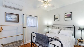 Um quarto com cama, duas mesas de cabeceira, um ventilador de teto e uma janela com cortinas.